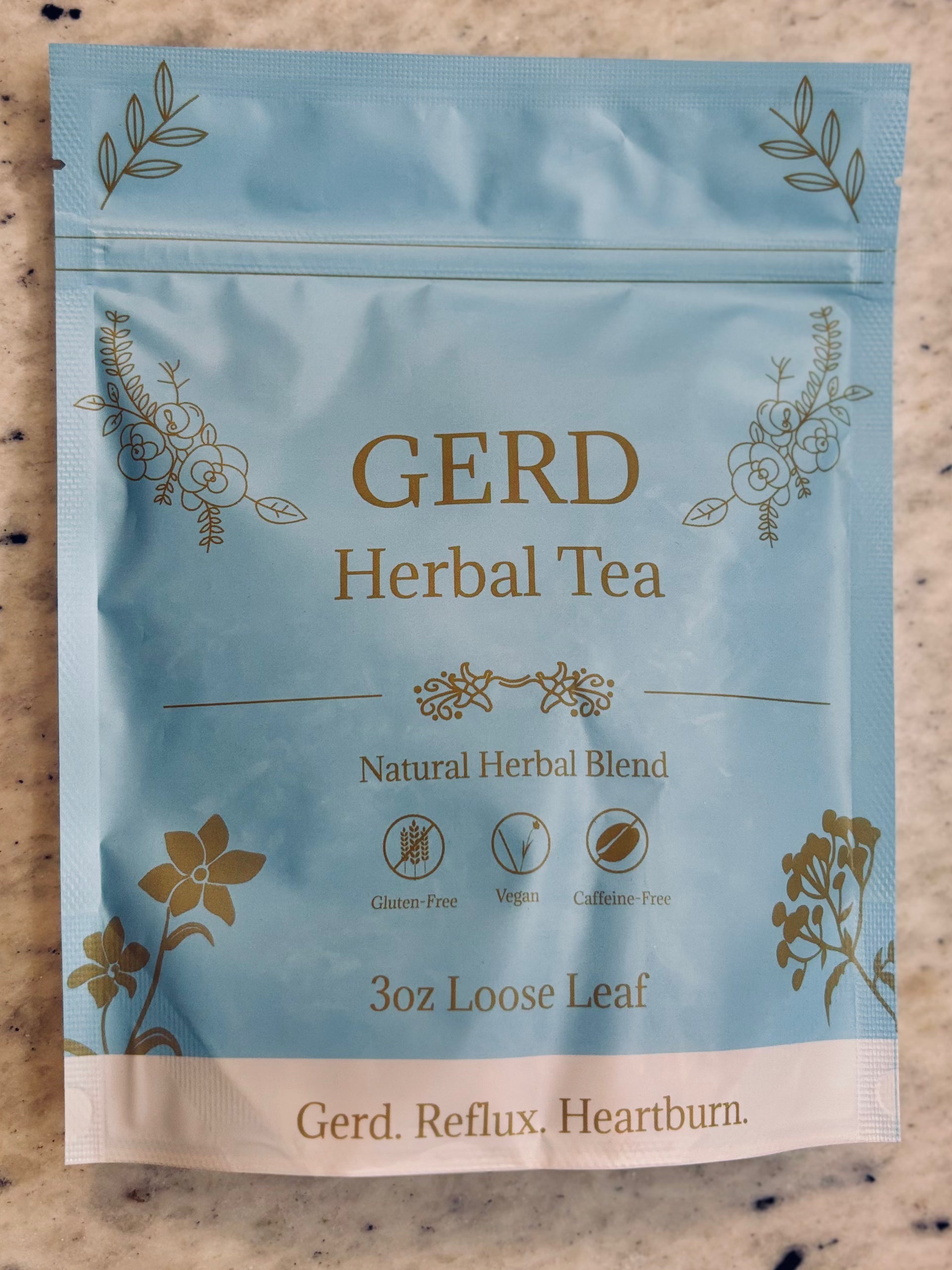 A 3 oz pouch of Gerd Herbal Tea on a speckled beige countertop. The packaging is light blue with gold foil botanical illustrations and text reading 'GERD Herbal Tea' and 'Gerd.